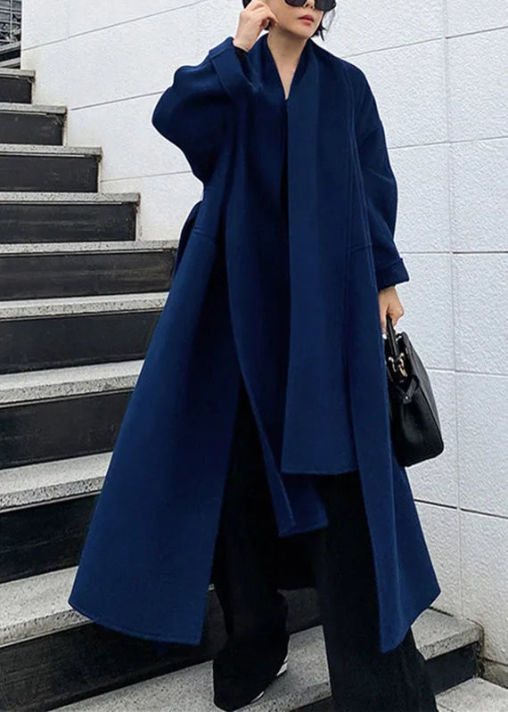 Full length view on stairs of the navy oversized coat with draped scarf collar, wide sleeves and floor-grazing hem