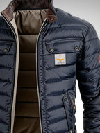 Detail of chest pocket, woven bull logo patch and ribbed cuffs on the navy quilted puffer jacket