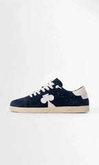 Side profile of navy suede trainer with white leather heel tab and clover-shaped side panel on a cream sole