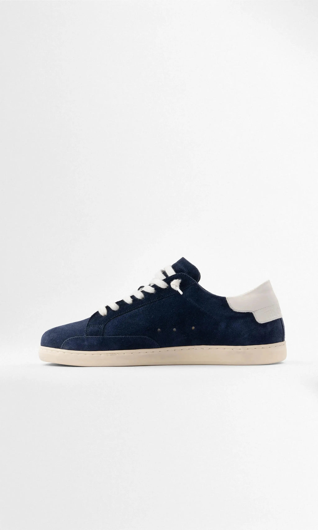 Full side view of the navy suede trainer showing the white heel panel with embossed branding and stitched sole detail