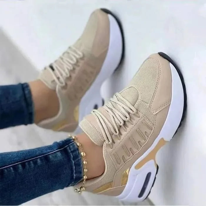 Beige and gold chunky trainers with lace-up front and white platform sole, shown on model's feet