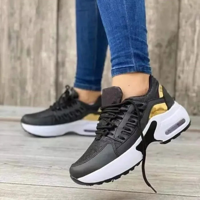 Black and gold chunky trainers with glittery panels and white air-cushion midsole, side view on foot