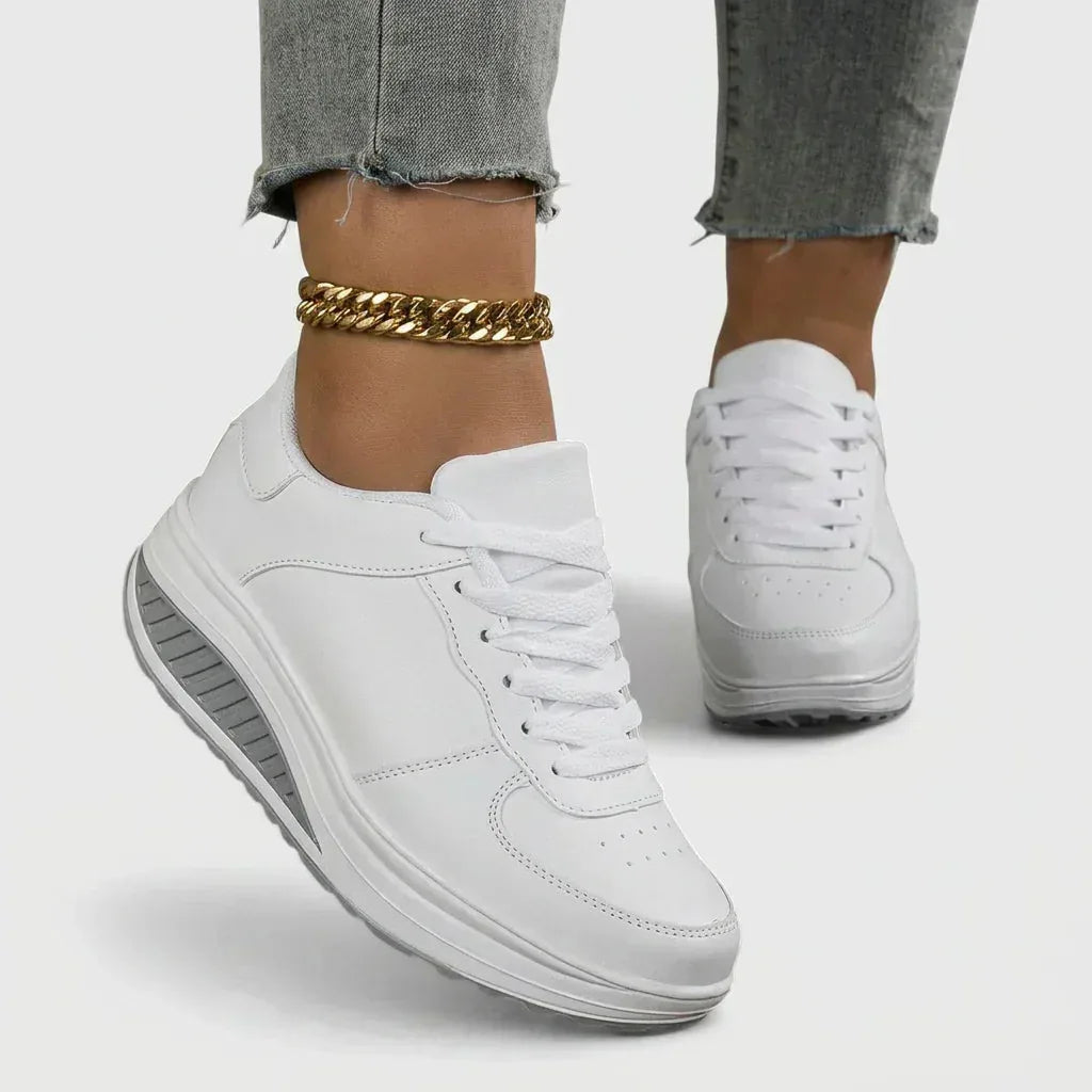 Side view of white lace-up trainers with grey wedge sole, worn with cropped jeans and a gold anklet