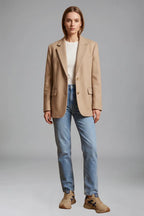 Woman styling beige trainers with light wash straight jeans and an oversized camel blazer