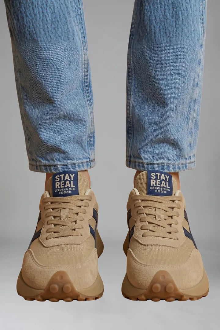 Front close-up of beige trainers worn with cropped jeans, showing navy heel tab branding