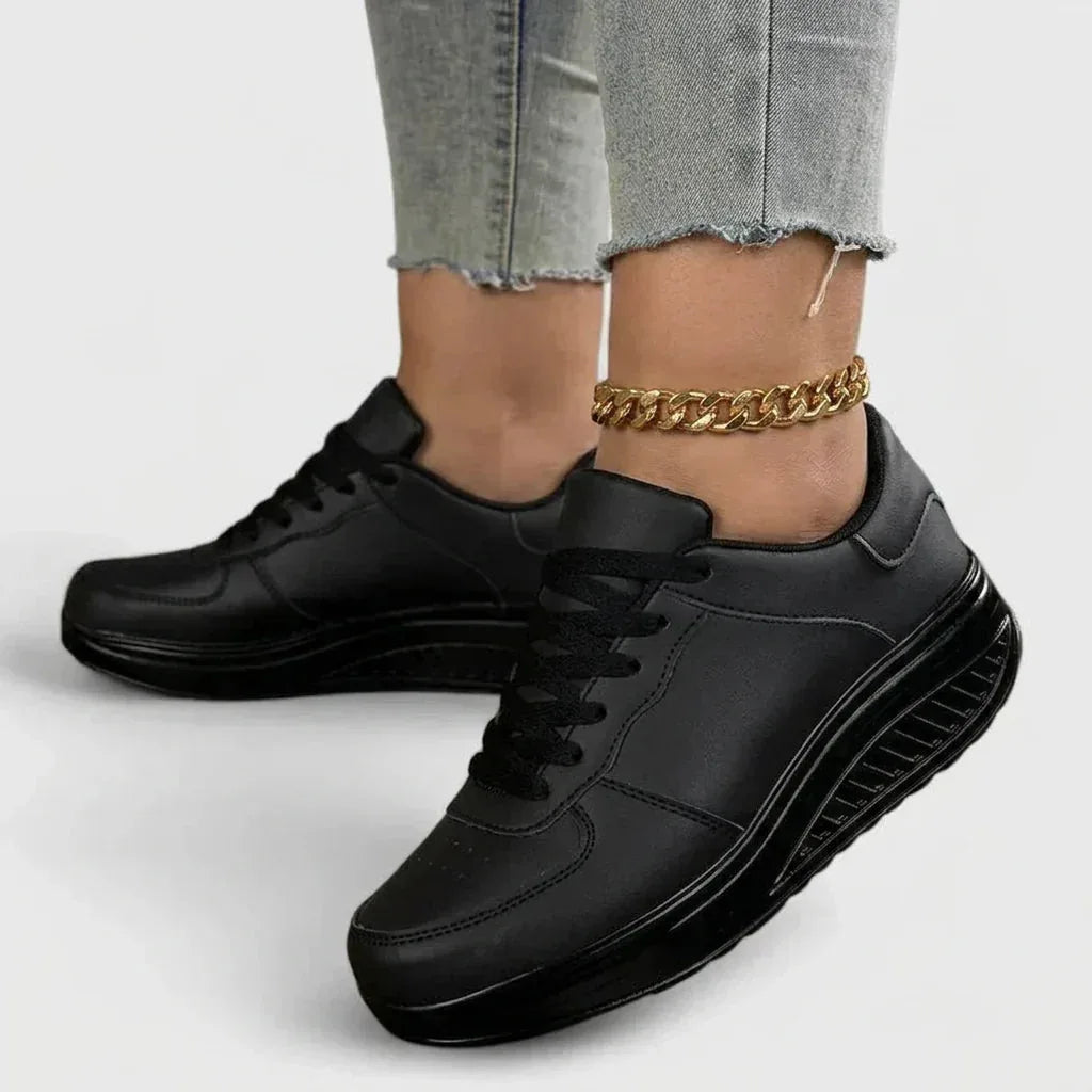Angled view of all-black lace-up trainers with a black platform wedge sole, worn with jeans