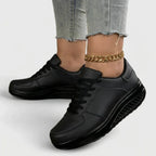 Angled view of all-black lace-up trainers with a black platform wedge sole, worn with jeans