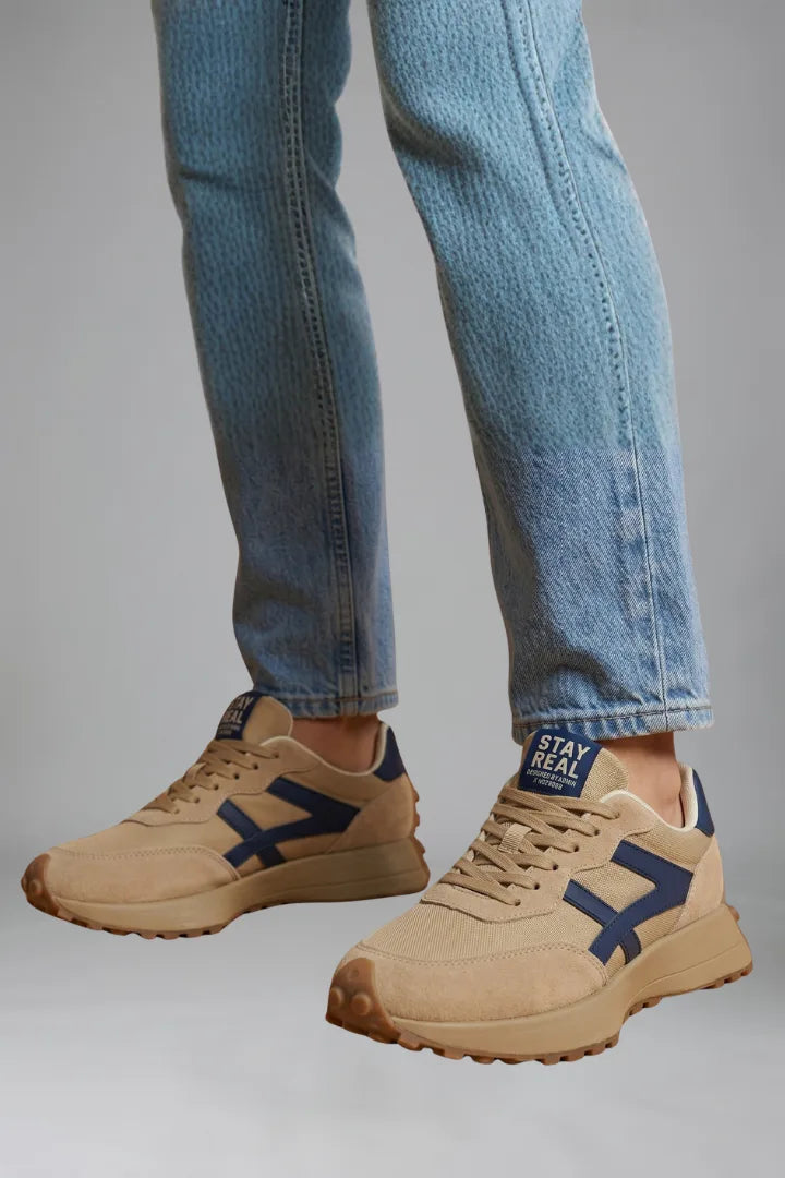 Side profile of beige trainers on foot with navy arrow-shaped panel and chunky tread sole