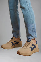 Side profile of beige trainers on foot with navy arrow-shaped panel and chunky tread sole