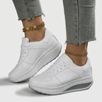 Pair of white lace-up trainers with textured grey wedge sole shown from the front, worn on both feet