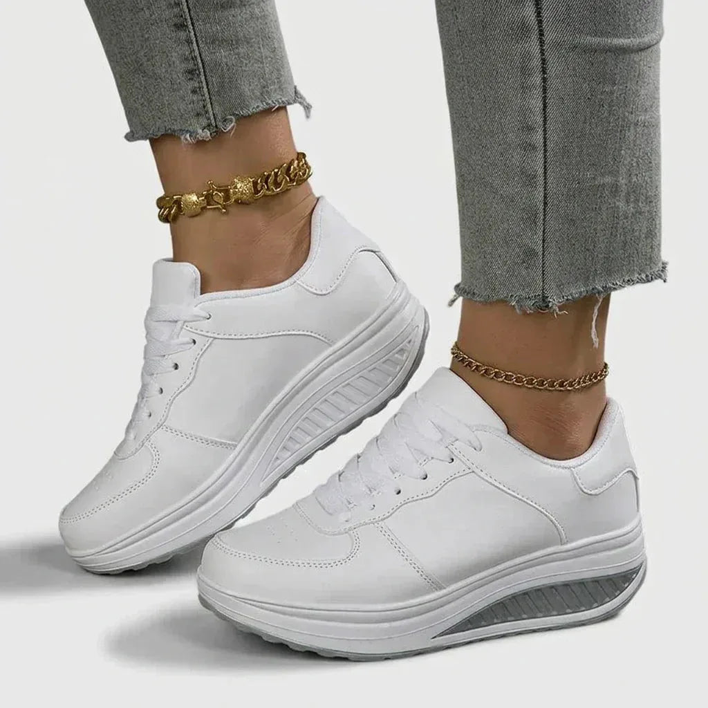 Pair of white lace-up trainers with textured grey wedge sole shown from the front, worn on both feet