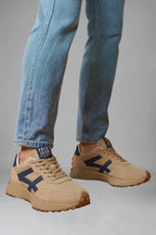 Angled view of beige trainers with navy detailing worn beneath rolled denim trousers