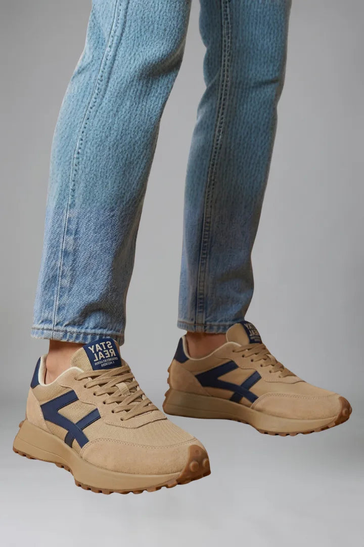 Angled view of beige trainers with navy detailing worn beneath rolled denim trousers