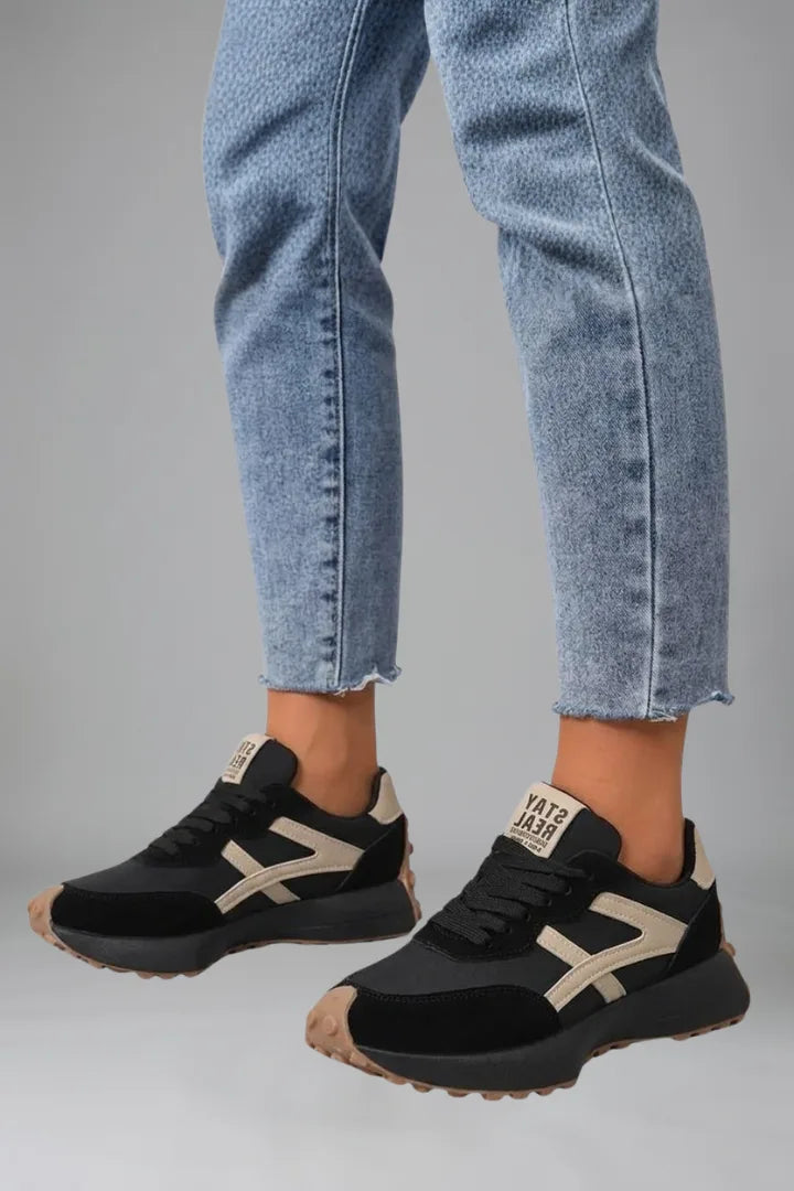 Close-up of black trainers with beige contrast arrow panel worn with cropped jeans