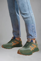 Close-up of green trainers with mustard contrast panel and navy heel tab on model's feet