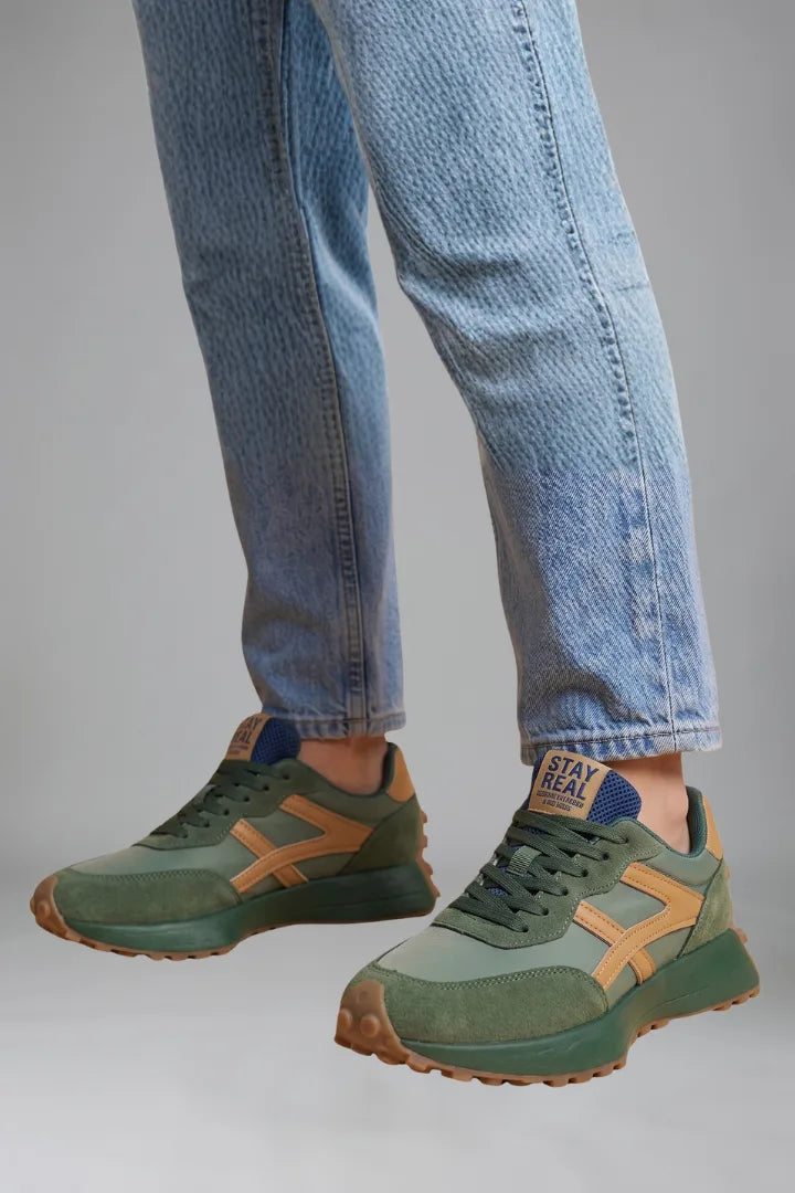 Close-up of green trainers with mustard contrast panel and navy heel tab on model's feet