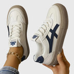 Side profile of a white leather trainer with navy stripe detail and thick beige sole, worn on foot