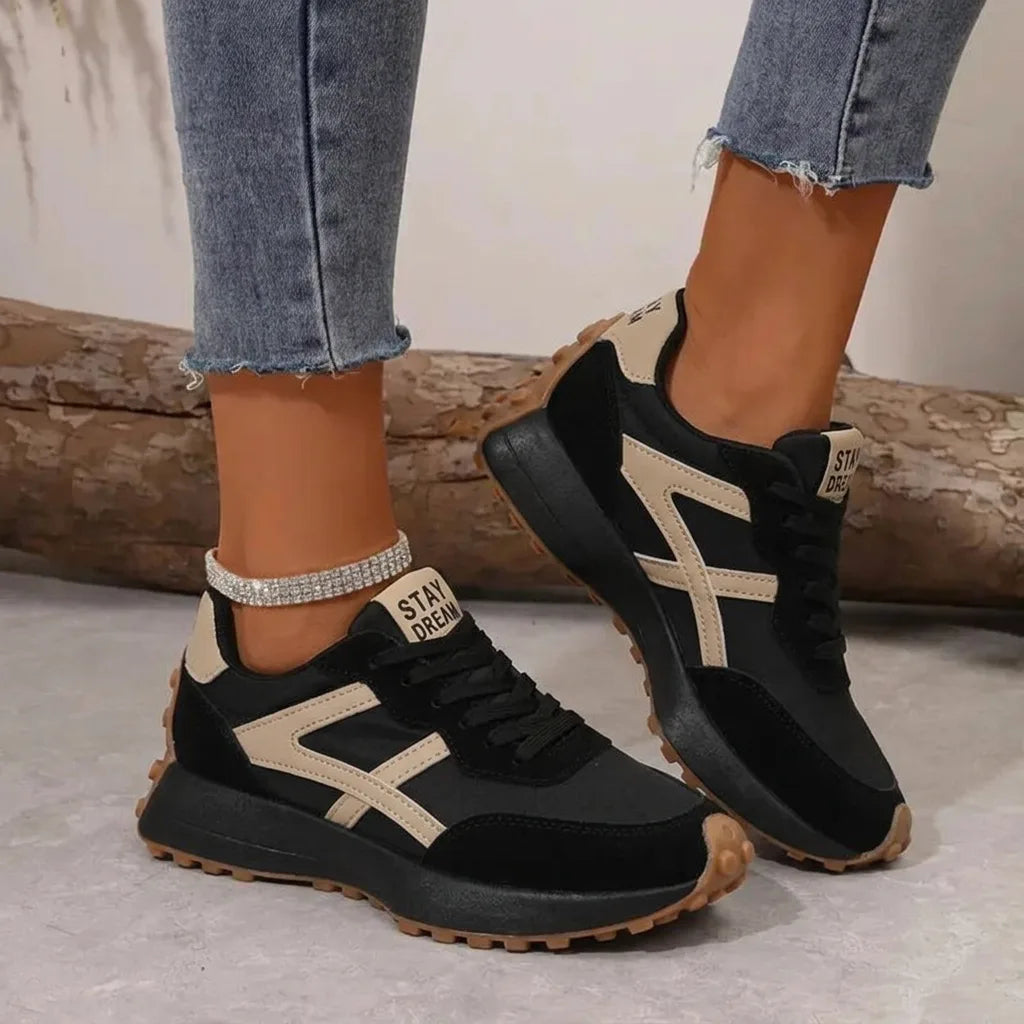 Black and beige panelled trainer with gum sole, shown from the side on a model's foot outdoors