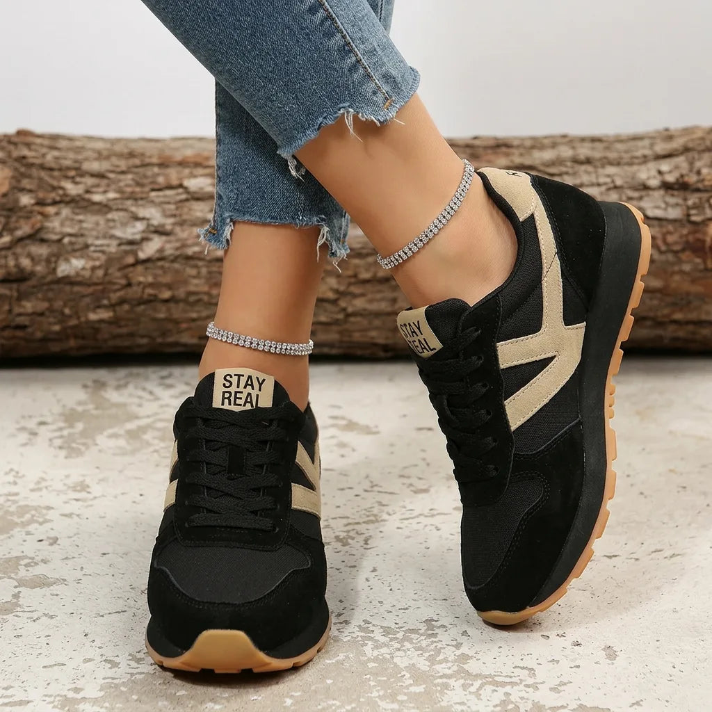 Close-up back view of black trainers with beige 'Stay Real' heel tab and contrasting side stripe
