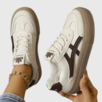 Two white trainers with navy stripe and beige sole held up and worn, showing sole tread and lining