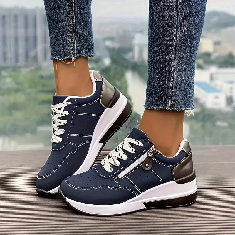 Side view of navy blue lace-up trainers with metallic heel panel and white wedge sole, worn with cropped jeans