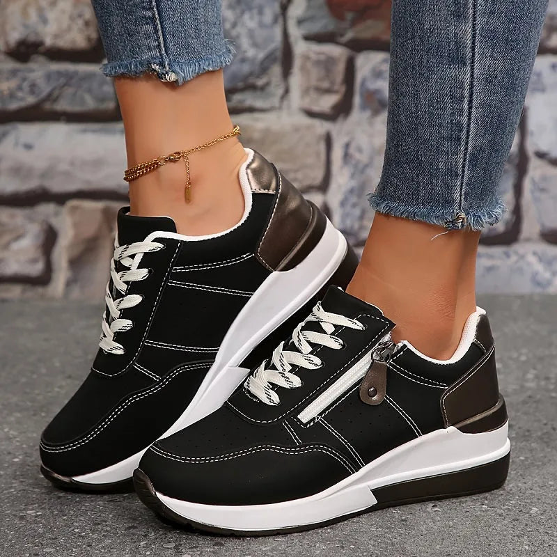 Close-up of black trainer with side zip fastening, contrast stitching and metallic heel panel detail
