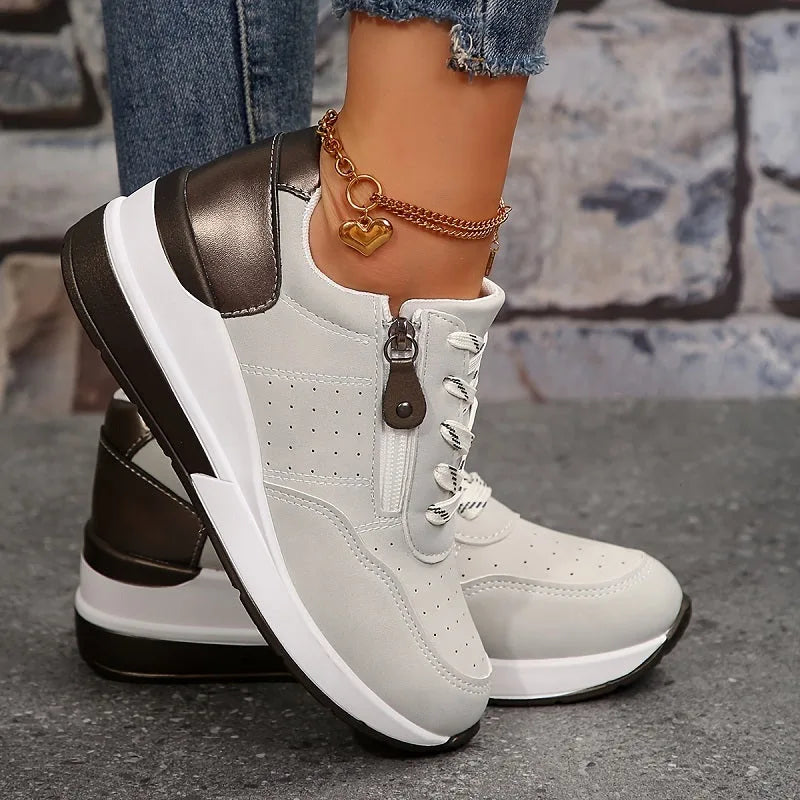Close-up side profile of black canvas-style trainers with white laces and layered wedge sole against stone