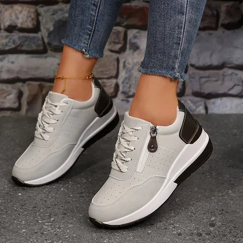 Pair of grey lace-up trainers with metallic heel trim, zip fastening and white sole worn with a gold anklet