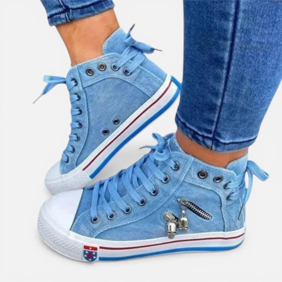 Side view of light blue denim high-top trainers with lace-up front and skull charm zip detail, worn with cropped jeans