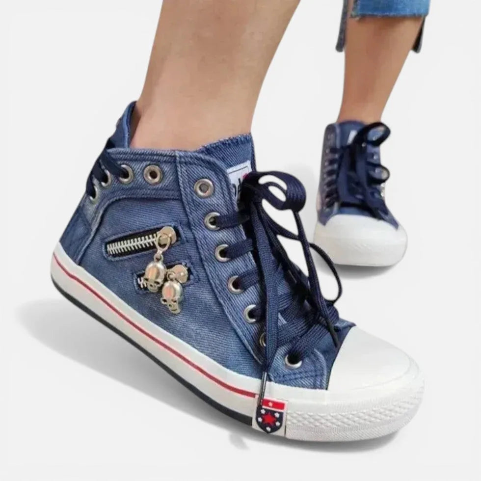 Angled view of navy denim high-top trainers showing the side zip pocket with skull charms and white rubber sole