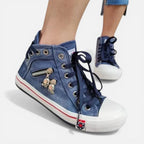 Angled view of navy denim high-top trainers showing the side zip pocket with skull charms and white rubber sole