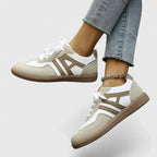 Side view of a khaki and white lace-up trainer with brown ridged sole, worn on foot with cropped jeans and an anklet