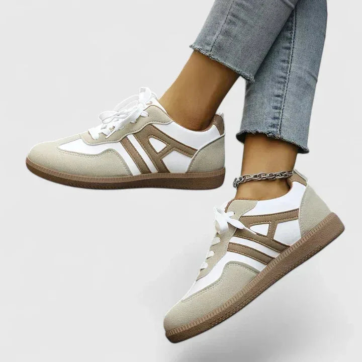 Side view of a khaki and white lace-up trainer with brown ridged sole, worn on foot with cropped jeans and an anklet