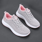 Pair of grey mesh trainers with soft pink lining, laces and sole accent, shown on a dark background