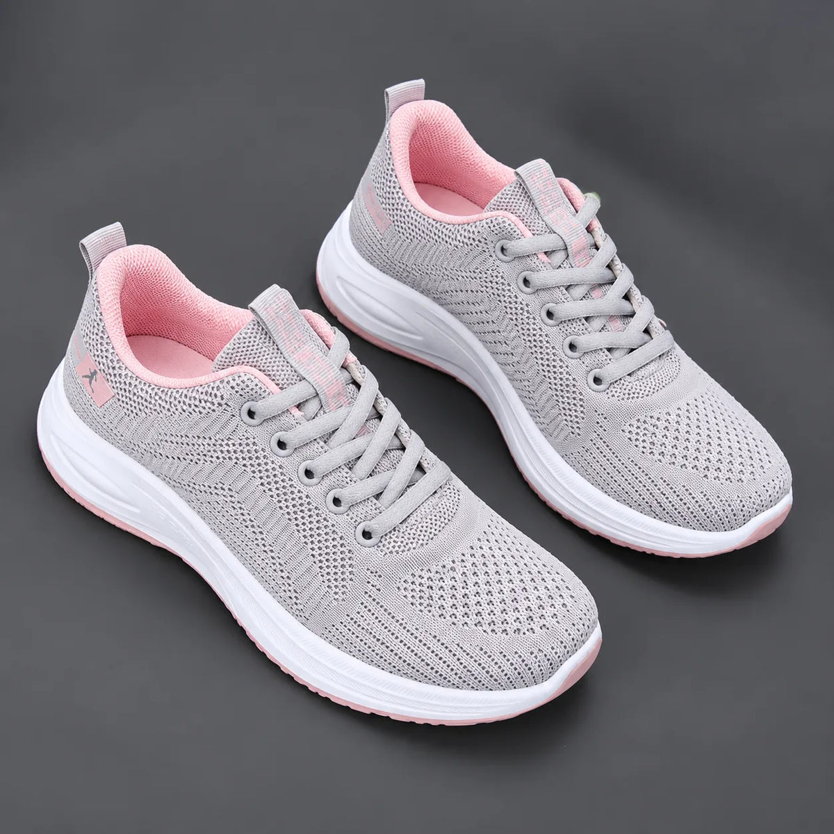 Pair of grey mesh trainers with soft pink lining, laces and sole accent, shown on a dark background