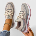 Beige and pink knit trainers with lace-up front and chunky sole, worn on foot with ankle jewellery