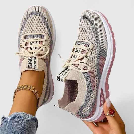 Beige and pink knit trainers with lace-up front and chunky sole, worn on foot with ankle jewellery