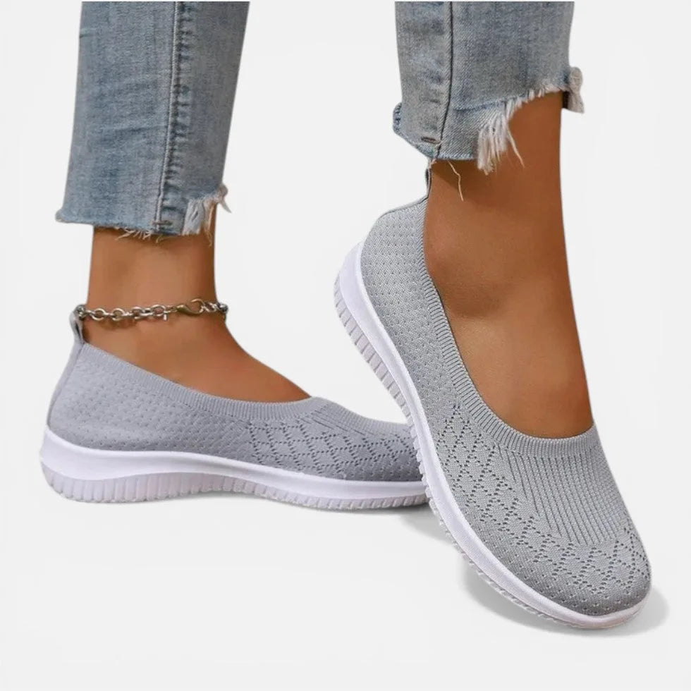 Grey knit slip-on trainer with white sole, worn on foot with cropped jeans and an anklet chain