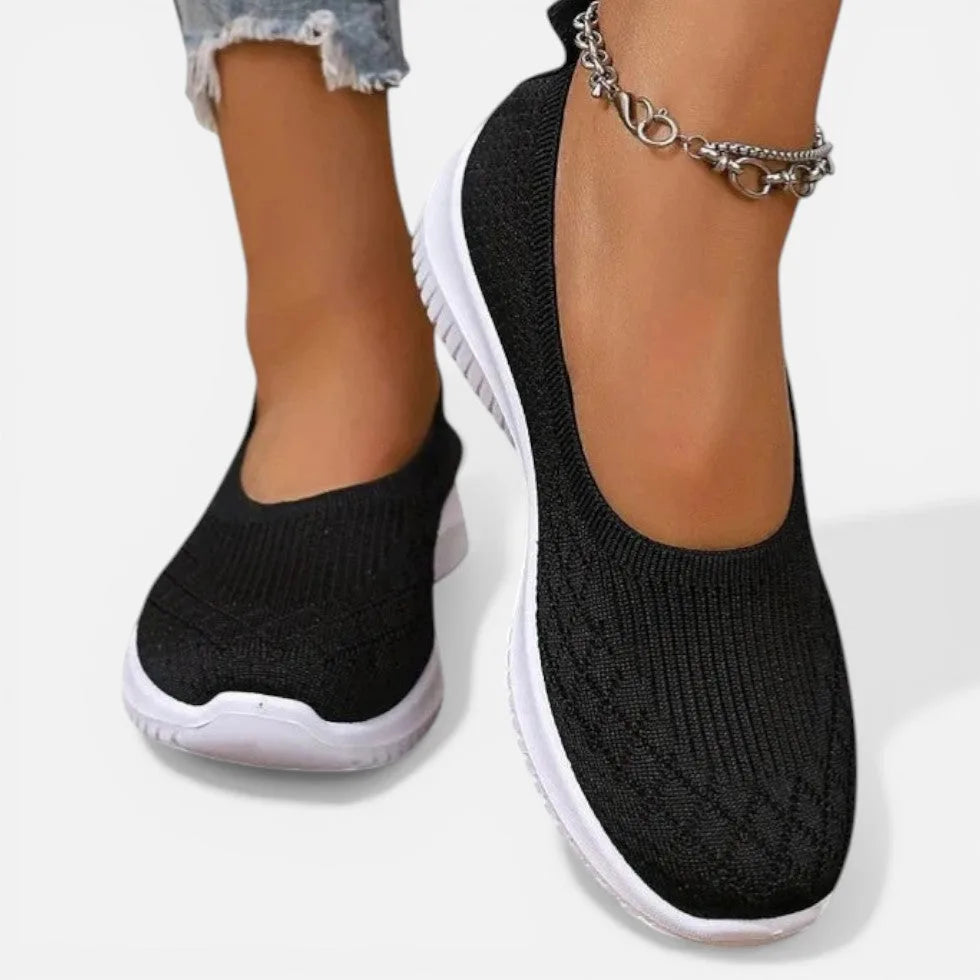 Shiny black knit slip-on trainer front angle, round toe and white outsole with silver anklet
