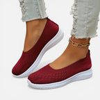 Red-orange knit slip-on trainer side view, ribbed collar and white sole against a light background
