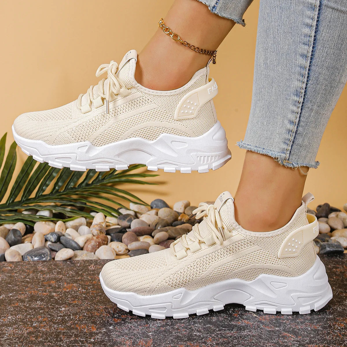 Side view of cream knit trainers with white chunky sole, worn with cropped jeans and a gold anklet