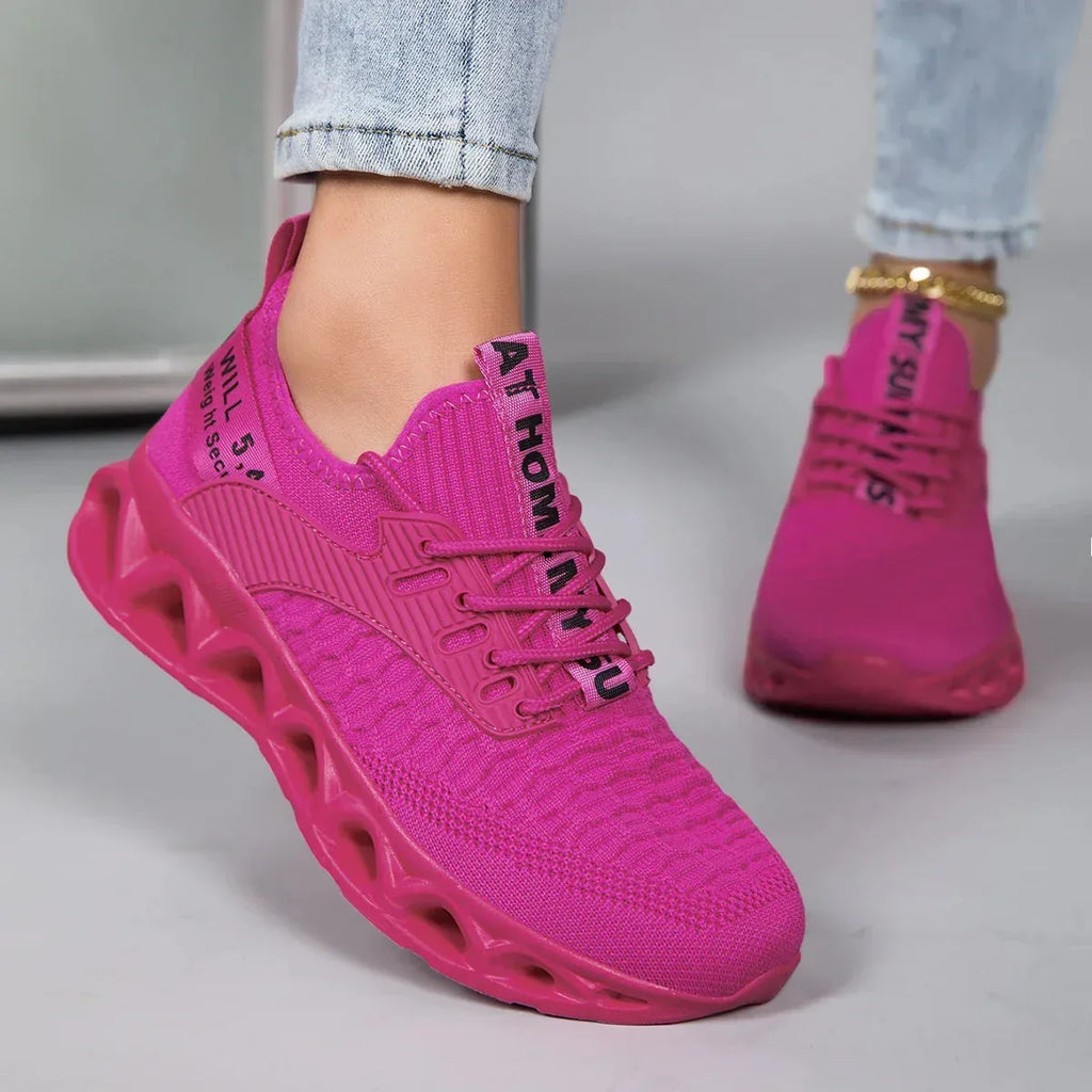 Side view of a hot pink knit trainer with ribbed panel, laces and blade-style cutout outsole, worn on foot