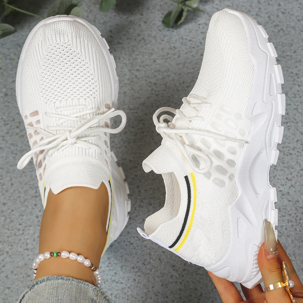 Overhead view of white knit trainers with white sole and yellow and navy stripe accents on the tongue