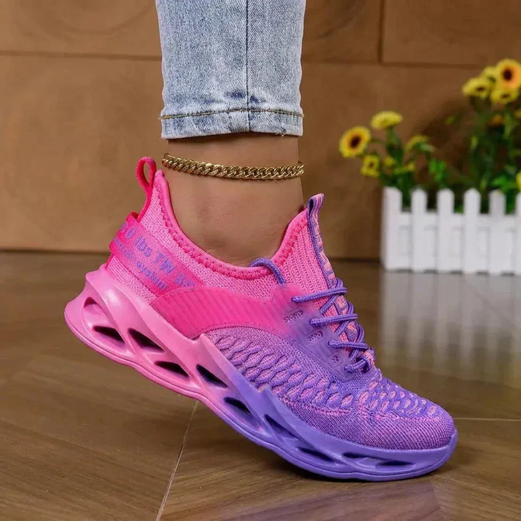 Pink and purple knit trainer worn on ankle with gold anklet, seen from behind near the heel loop