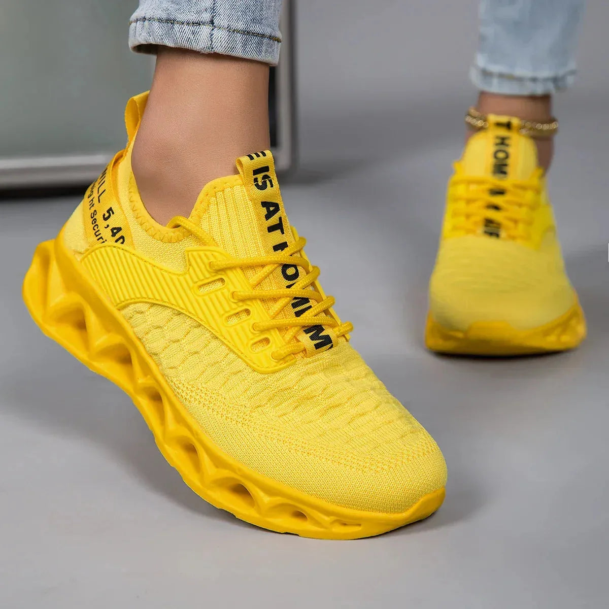 Side angle of a yellow knit trainer with contrast black lace-up panel and textured sole, worn while walking