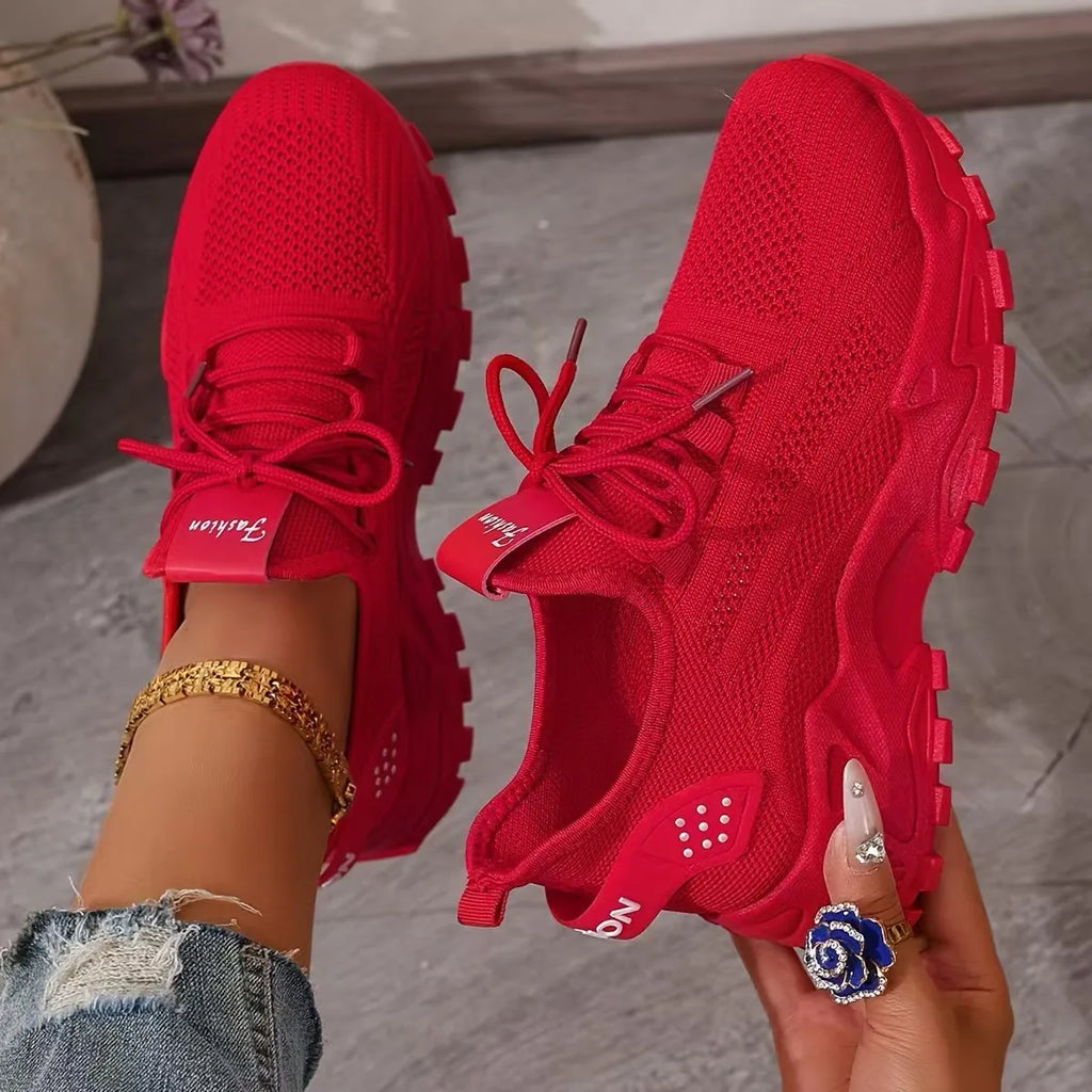 Close-up of red knit trainers with red chunky sole and fabric heel loop, worn with ripped jeans