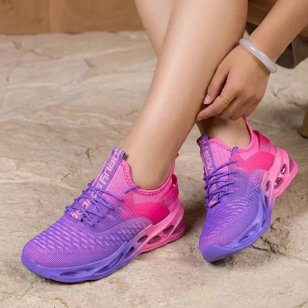Close-up side view of pink to purple gradient trainer resting on stone ground, showing mesh knit texture