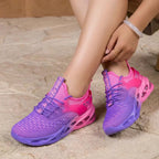 Close-up side view of pink to purple gradient trainer resting on stone ground, showing mesh knit texture