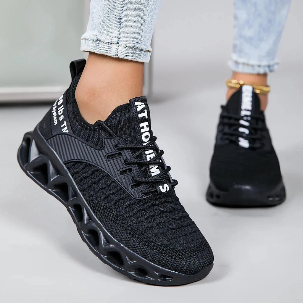 Close-up side view of an all-black knit trainer with white text detailing and chunky cutout sole