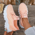 Overhead view of peach knit trainers with white chunky sole and lace-up front on a wooden surface